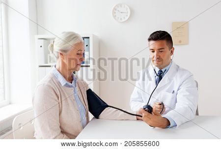 medicine, age, healthcare and people concept - senior woman patient and doctor with tonometer measuring blood pressure at hospital