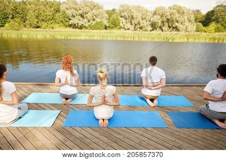 fitness, sport, yoga and healthy lifestyle concept - group of people exercising in reverse prayer pose on river or lake berth
