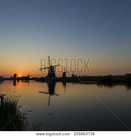 Travel Concepts. Picturesque Image of Historic Dutch Windmills In Front of The Canal Located in Traditional Village in Holland The Netherlands. Shot at Kinderdijk During Golden Hour. Square Image