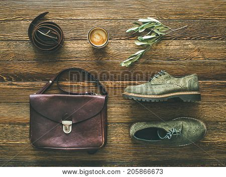Flat-lay of woman's fall accessories and coffee. Haki suede oxford boots, brown shoulder bag, leather belt and cup of espresso over wooden background, top view