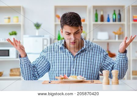 Young husband eating tasteless food at home for lunch
