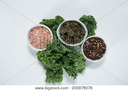 Overhead view of salt and peppercorn with kale on white background