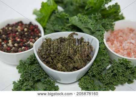 Close up of peppercorn and salt with kale against white background