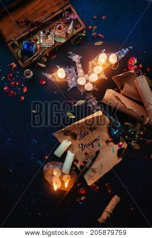 Fantasy still life with a dragon made of candle flame, spell scrolls, herbs, potion bottles and rose petals. Witch or wizard workplace, Halloween and occult concept. Dark magical flat lay.
