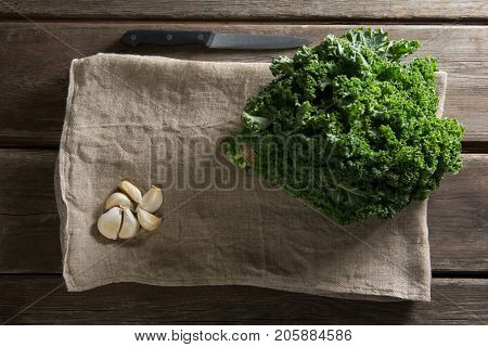 Overhead view of fresh kale leaves with garlic on napkin at wooden table