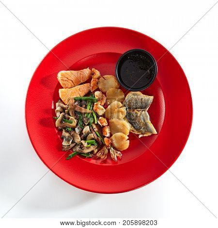 Teppanyaki Japanese and Korean Grill Food - Salmon, sea bass, shrimp 6/8, sea scallop garnished with vegetables sauce and spices on red plate on white isolated background. Asian menu. Top View