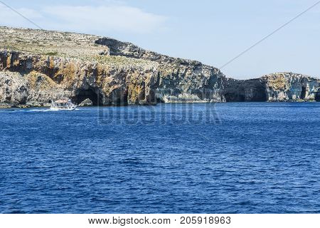 Comino is a small island of the Maltese archipelago between the islands of Malta and Gozo in the Mediterranean Sea. Pleasure craft at the rugged coastline delineated by sheer limestone cliffs and dotted with deep caves