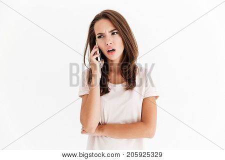 Confused brunette woman talking by the smartphone over white background