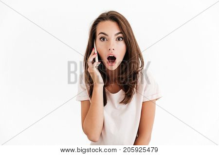Shocked brunette woman talking by the smartphone and looking at the camera over white background