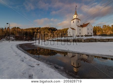 Church in march, winter landscape with snow and blue sky in Iveland in the south part of Norway. Reflections of the church in water