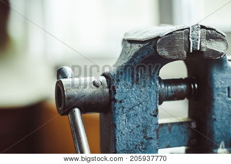 Close up on a red tabletop mounted vise grip with screw action grip and cast iron frame in a machining workshop