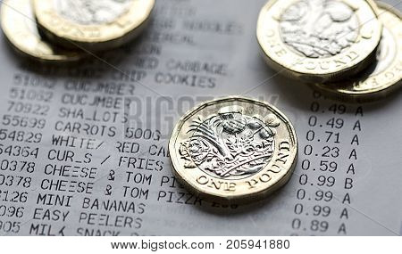 One pound coins on a grocery till reciept with an itemised list of food and prices with focus on the foreground.