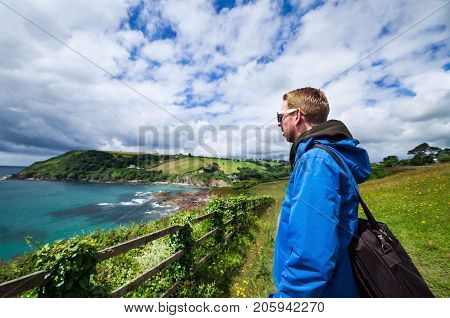 Young man in a blue jacket is gazing over the blue waters of Talland Bay on a sunny summers day in South Cornwall, England.