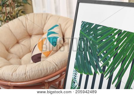 Framed picture of tropical leaves and papasan chair indoors