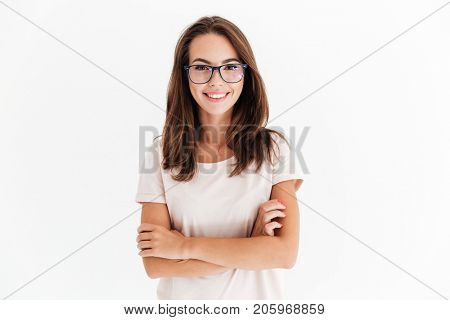 Smiling brunette woman in eyeglasses posing with crossed arms and looking at the camera over white background