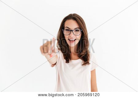 Happy brunette woman in eyeglasses pointing at the camera over white background