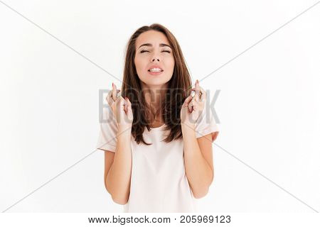 Pretty brunette woman prays for luck with closed eyes over white background