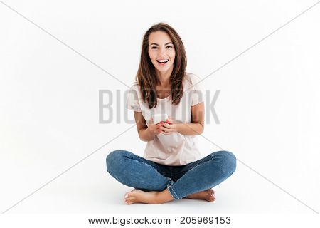 Happy brunette woman holding smartphone in hands and looking at the camera over white background