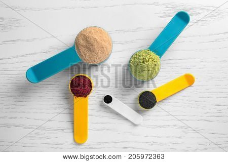 Composition with various colorful superfood powders and measuring spoons on wooden background