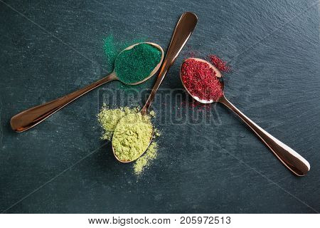 Various colorful superfood powders in spoons on color background
