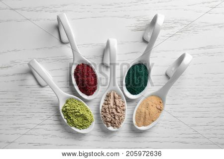 Various colorful superfood powders in white ceramic spoons on wooden background