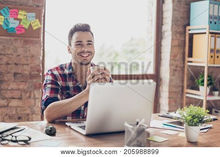 Low Angle Shot Of Successful Happy Brunet Student, Sitting With Cup Of Tea, Smiling, In Front Of Com