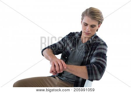 Businessman looking at imaginary wristwatch while sitting on chair against white background