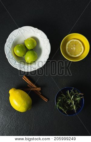 Overhead view of ctrus fruit, cinnamon sticks and rosemary on black background