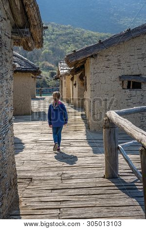 Little Caucasian Girl Walking Among Mud And Straw Houses In The Bay Of The Bones Museum On Water, Au