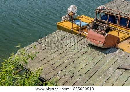 Abandoned Yellow Fishing Boat With Outboard Motor Filled With Dirty Water And Trash Docked At Wooden