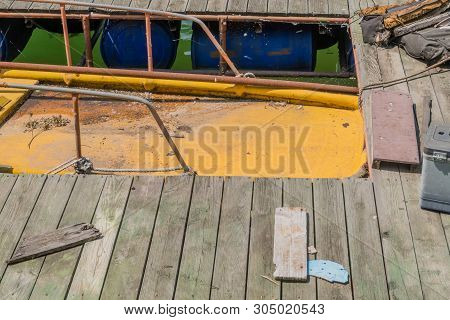 Abandoned Yellow Fishing Boat Filled With Dirty Water Docked At Wooden Pier Littered With Debris.