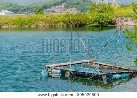 Old Abandoned Fishing Dock Floating On Blue Metal Drums In Lake On Sunny Day.