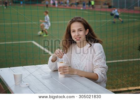 High School Student Drinking Coffee On Summer Terrace Of School Cafe. She Is Smiling And Posing For 
