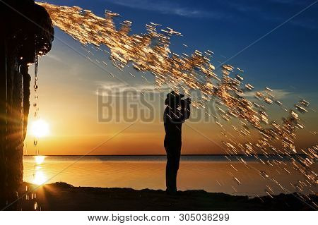A Man Photographs The Sunset Over The Water On The Background Of Golden Splashes Of Water.