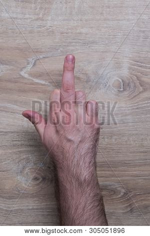 Male Hand The Gesture Of The Fuck. Hand Shows A Fuck Sign. Hand On Wooden Background.