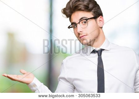 Young business man wearing glasses over isolated background Smiling showing both hands open palms, presenting and advertising comparison and balance