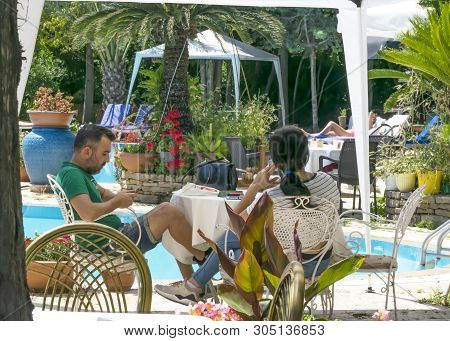Cyprus - May 31, 2019: Young Couple Relaxing Sitting At A Table In An Outdoor Restaurant With A Pool
