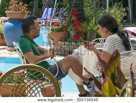 Cyprus - May 31, 2019: Young Couple Relaxing Sitting At A Table In An Outdoor Restaurant With A Pool