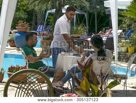 Cyprus - May 31, 2019: Young Couple Sitting At A Table In An Outdoor Restaurant With A Pool And Flow