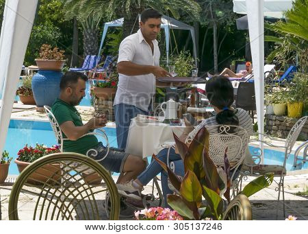 Cyprus - May 31, 2019: Young Couple Sitting At A Table In An Outdoor Restaurant With A Pool And Flow
