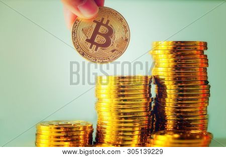 Hand Hold A Single Bitcoin Over Stack Of Glod Bitcoins, Cryptocurrency Concept. Virtual Currency Dig