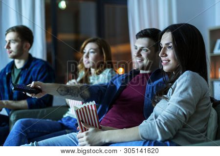 friendship and leisure concept - friends with popcorn and remote control watching tv at home at night