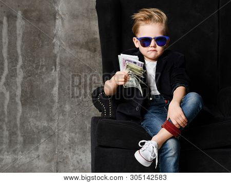 Portrait Of Self-confident Rich Kid Boy Millionaire Siting In Luxury Armchair With Bundles Of Dollar