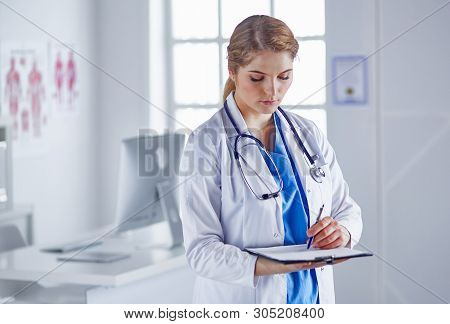 Young Woman Doctor Is Standing With Board With Clipboard Smilin