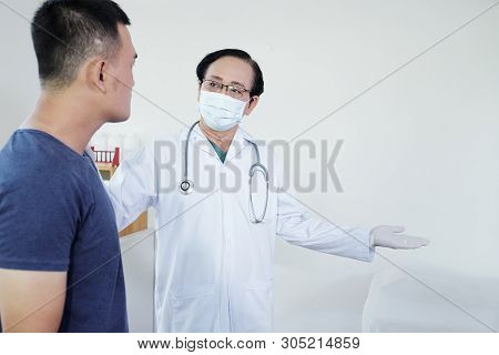 Senior General Practitoner In Medical Mask Asking Patient To Sit On Bed
