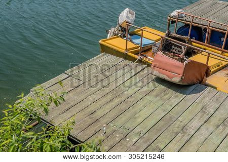 Abandoned Yellow Fishing Boat With Outboard Motor Filled With Dirty Water And Trash Docked At Wooden