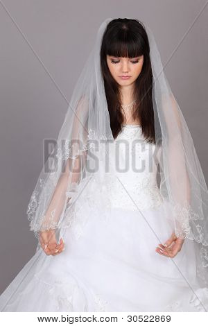 schöne melancholische Braut gekleidet in weißen Kleid schauen auf grauem Hintergrund