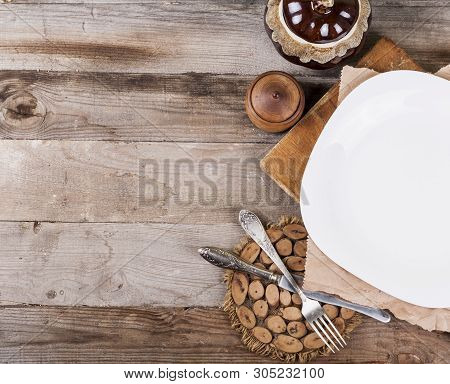 Light empty plate with kitchen accessories on a wooden background in vintage style.