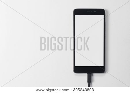 Smartphone With A Black Body And A Blank White Screen Display And A Data Cable Connected From The Bo