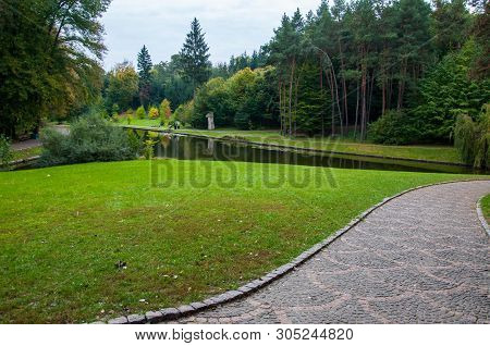 Patterned Stone Pathway Near Fresh Green Trimmed Lawn With Calm Pond And Tree Forest On Background. 